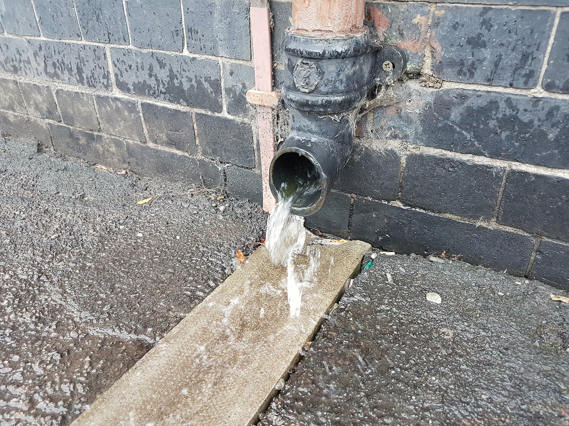 Water discharging from a downpipe during heavy rain, the point where roof water becomes a site problem.